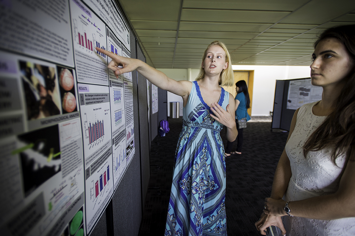 Student presenting her research poster to another student.